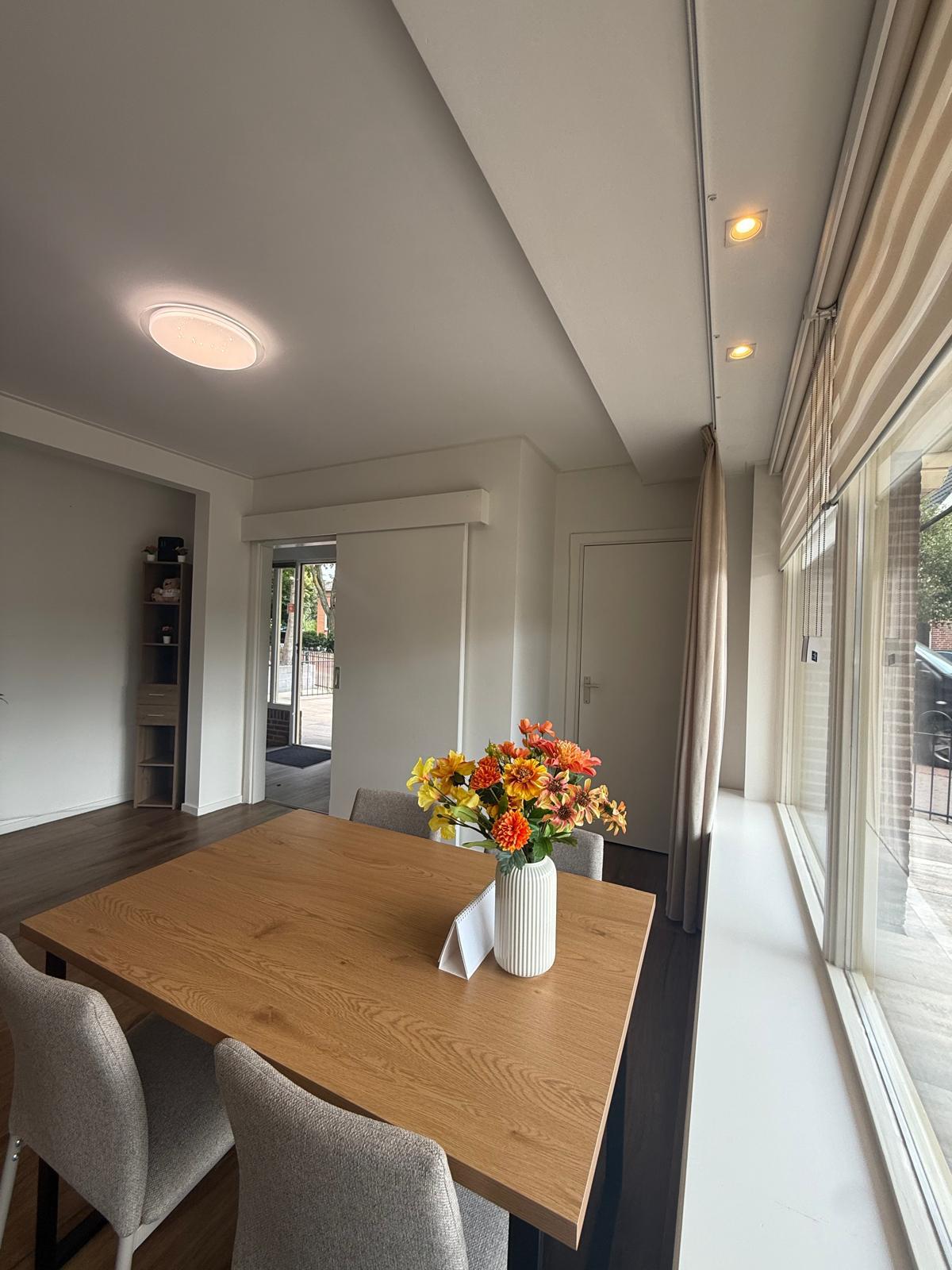 Lichte eetkamer met grote ramen en bloemen op tafel