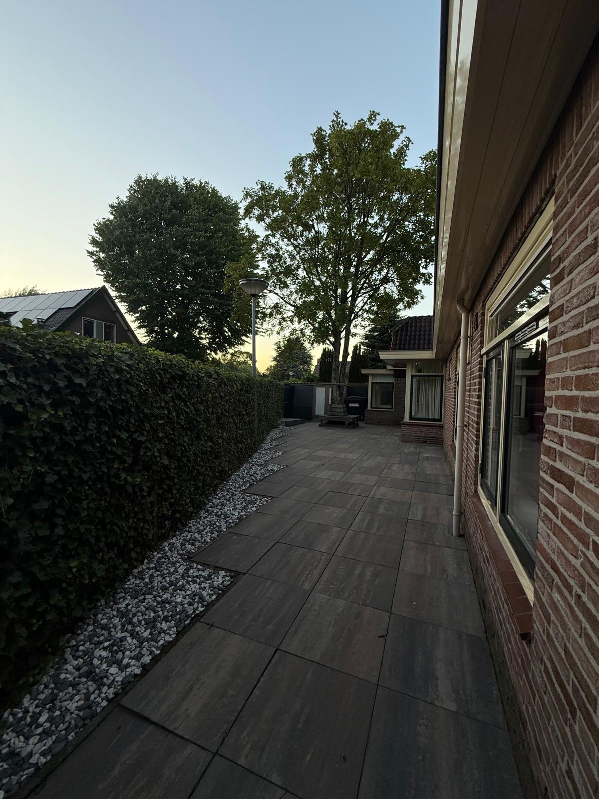 Beschut terras langs het gebouw met groene haag